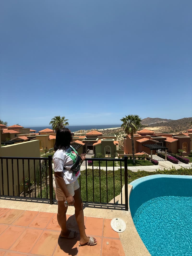Mima seen from behind on a terrace overlooking a pool, palm trees and the sea